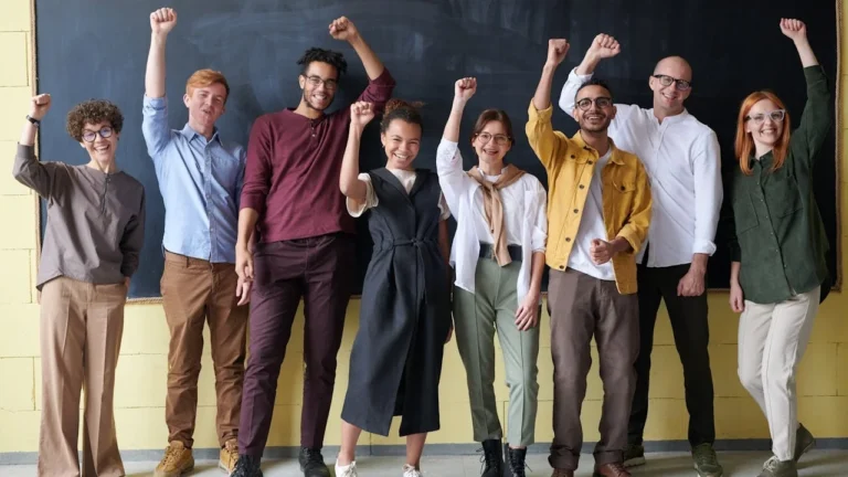 Children enthusiastically raising their hands in front of the classroom board