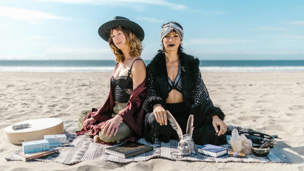 Decline of Christianity: Two women sitting on the beach on a blanket with books, a drum, a skull, and a Buddhist singing bowl