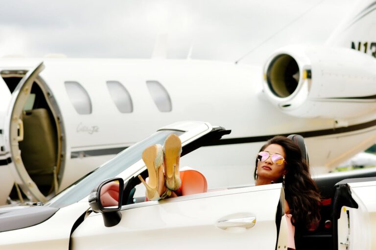 Climate change and hypocrisy: a woman relaxing in a luxury convertible car with her feet up, wearing high heels, and sunglasses, parked near a private jet with its door open in the background.