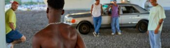 Crime in Sweden: A shirtless young man approaches a group of four casually dressed men standing near a car under a bridge.