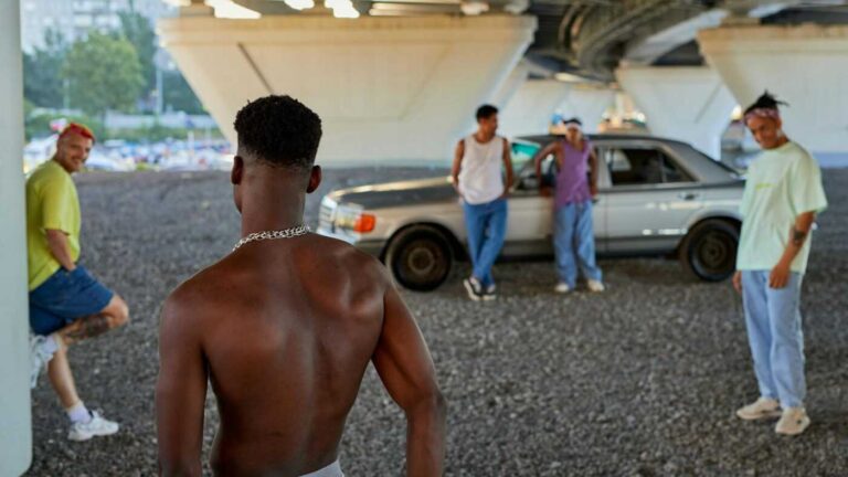 Crime in Sweden: A shirtless young man approaches a group of four casually dressed men standing near a car under a bridge.