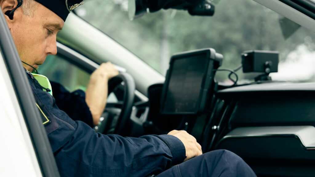 Crime in Sweden: A Swedish police officer in uniform sits inside a patrol car, focusing on the dashboard and onboard computer.