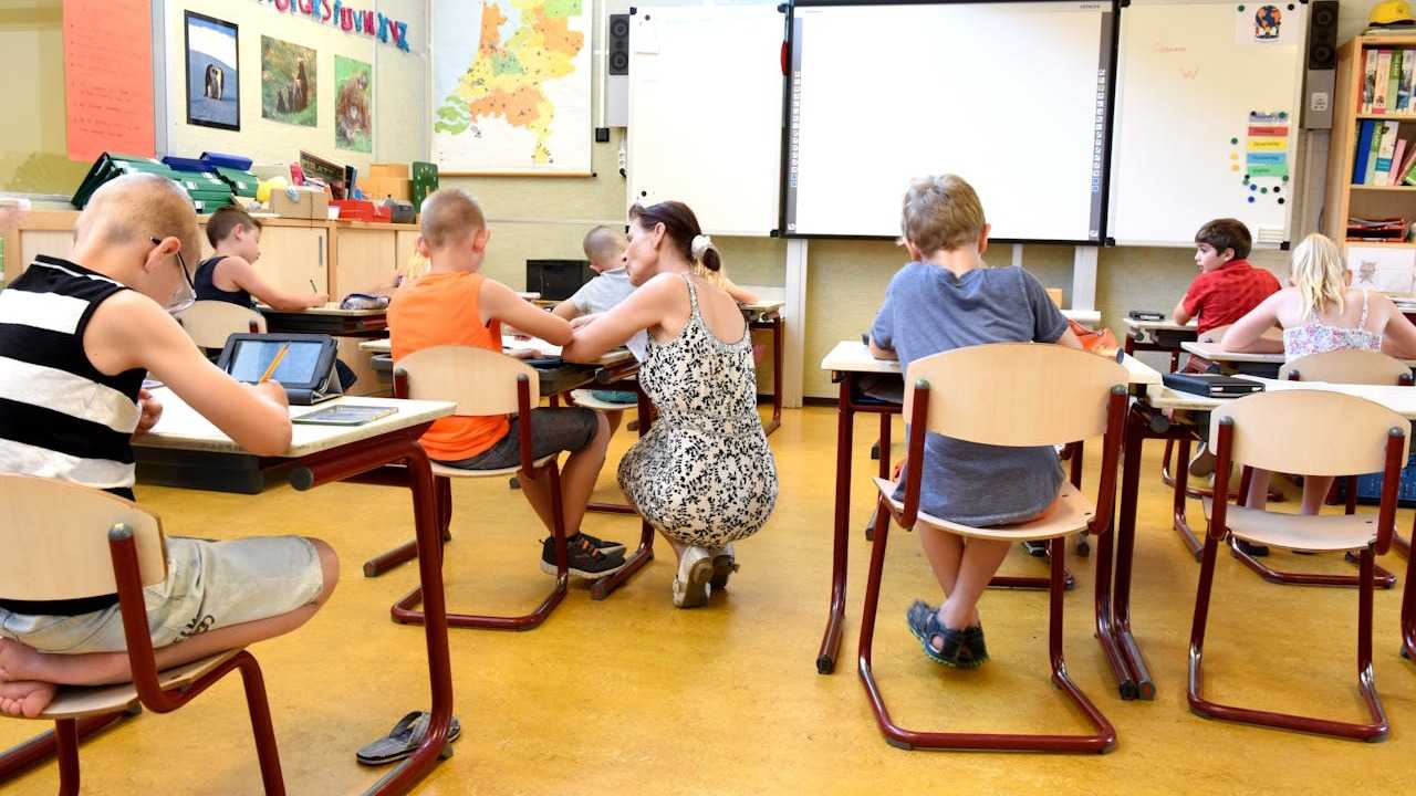School without Grades: a teacher is crouching next to a young child in a classroom