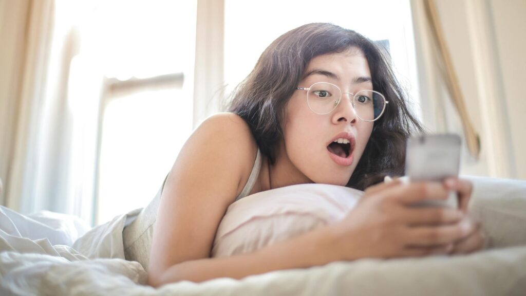 Send nudes culture: a shocked young girl on her bed is looking at something on her smartphone