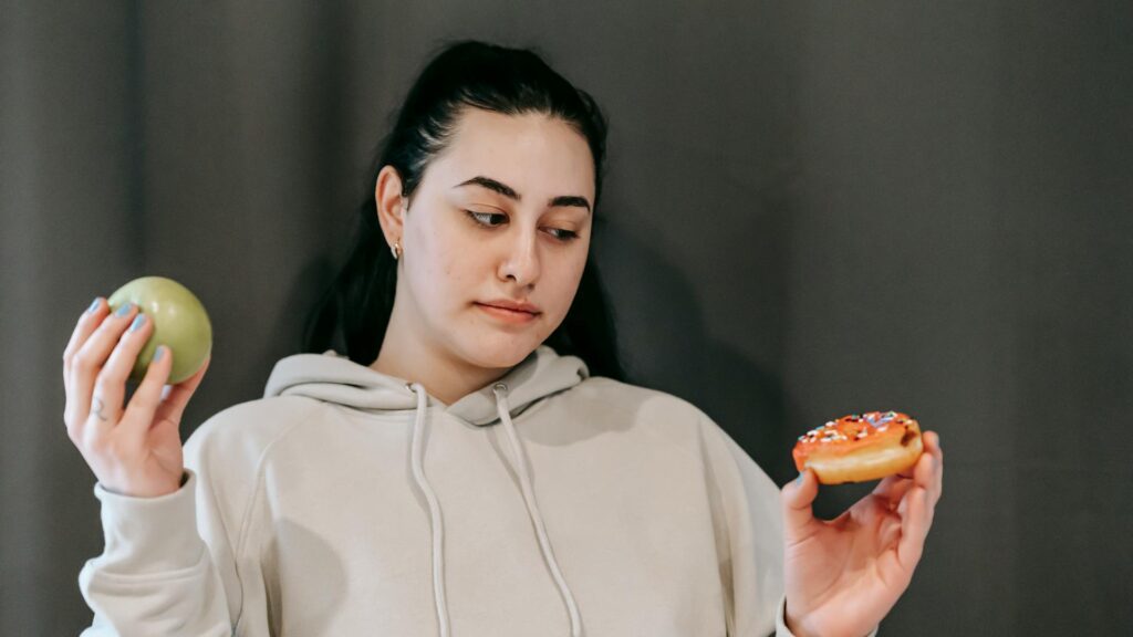 Success in life: A young woman is holding an apple in her right hand but is ogling a doughnut in her left hand