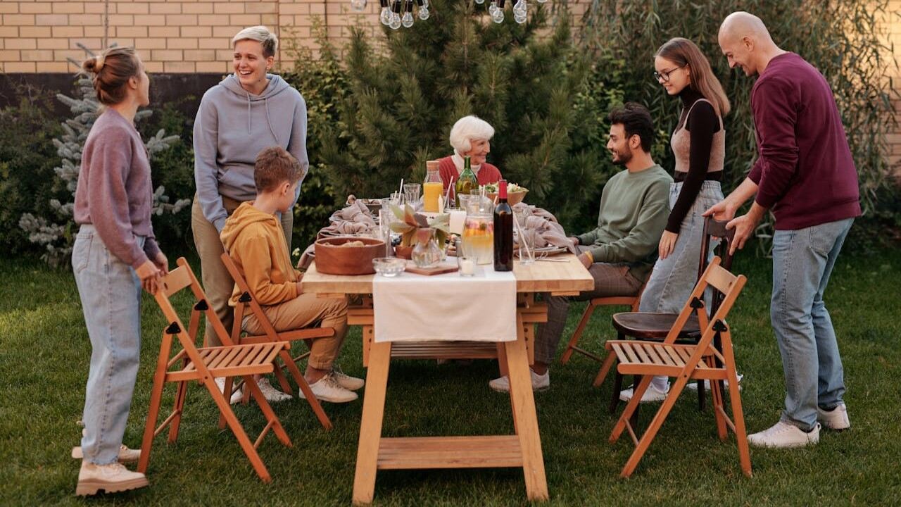 Family History: A multigenerational family gathered around a table outdoors, enjoying a meal together in a garden setting.