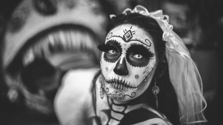 Fear and the Brain: a person in black and white with intricate Dia de los Muertos face paint, wearing a veil, with a large, blurred, open-mouthed figure in the background.