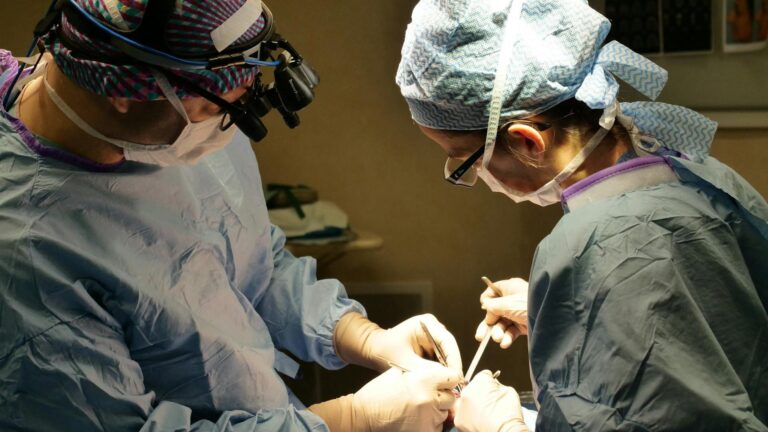 Medical Breakthroughs: Two surgeons in full surgical attire and masks perform an operation under bright surgical lights.