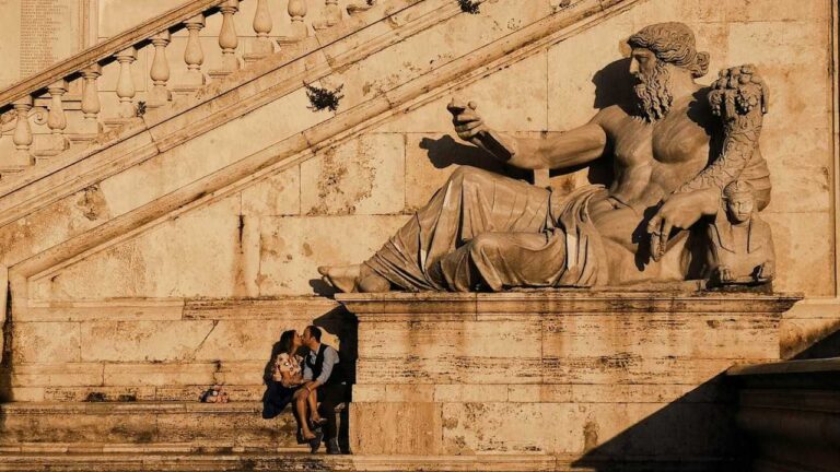 Philosophy at School: A couple sitting and kissing at the base of a grand stone statue on an ancient staircase.