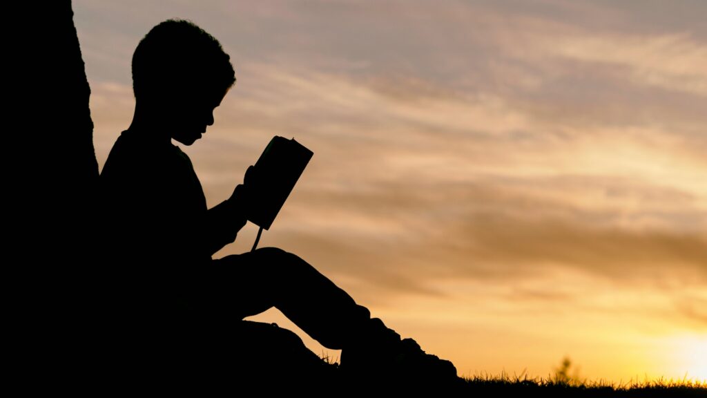 Philosophy at School: A silhouette of a child sitting under a tree, reading a book at sunset.