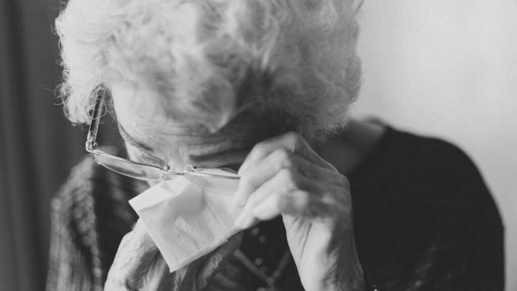 Senior Loneliness: an elderly woman tries to wipe her tears with a tissue