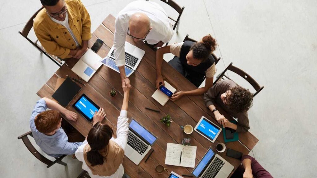 Working in a Group: overhead shot of a team meeting at work, at a table. A man and a woman shake hands.