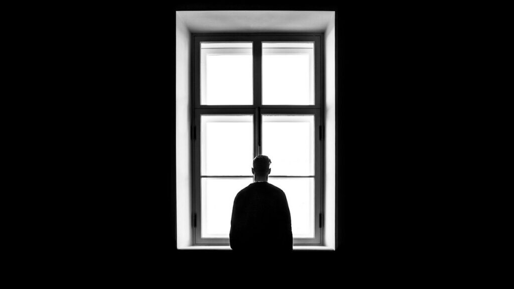 The Disenchanted World: A person stands alone in silhouette, facing a large, bright window in an otherwise dark room.