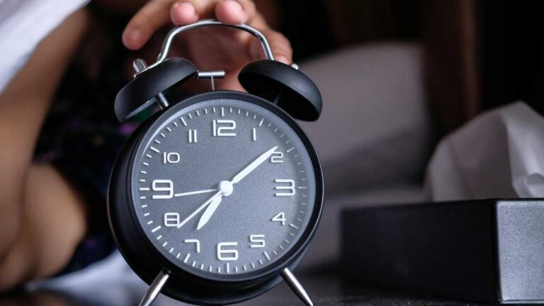How to sleep better. Photo: Towfiqu barbhuiya/pexels. A hand reaches for a clock just after waking up.