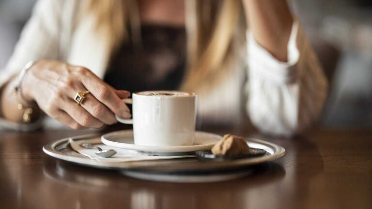 Coffee extends life. Photo: Engin_Akyurt/pixabay. Close-up of an elegant coffee cup on a silver tray, held by a woman in a light-colored jacket.