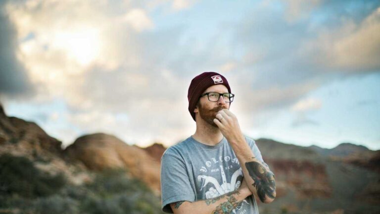 Intelligence and genes. A man in a cap and glasses stands thoughtfully against a mountainous landscape. Fot. Kitera Dent/Unsplash