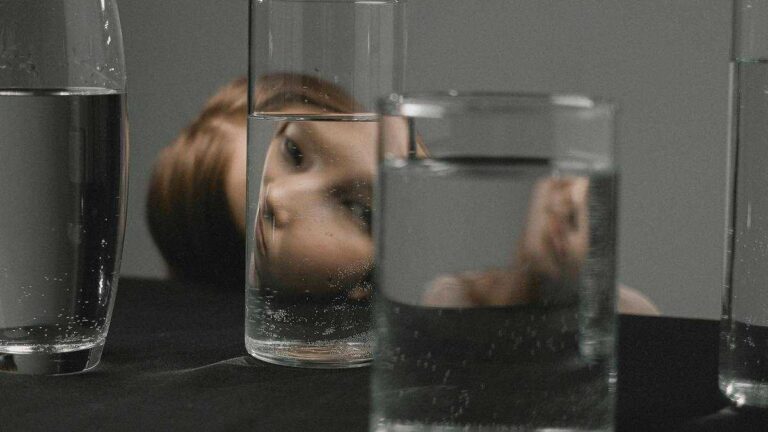 Common cognitive biases A woman looks through a row of water-filled glasses, where her distorted face is reflected.