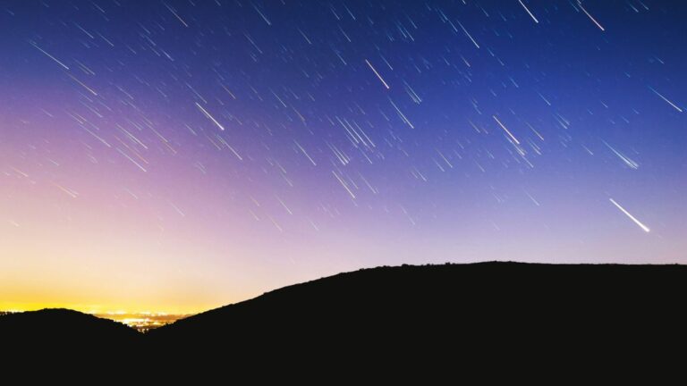 Perseids in 2025: a colorful sky with shooting stars and a dark ground.