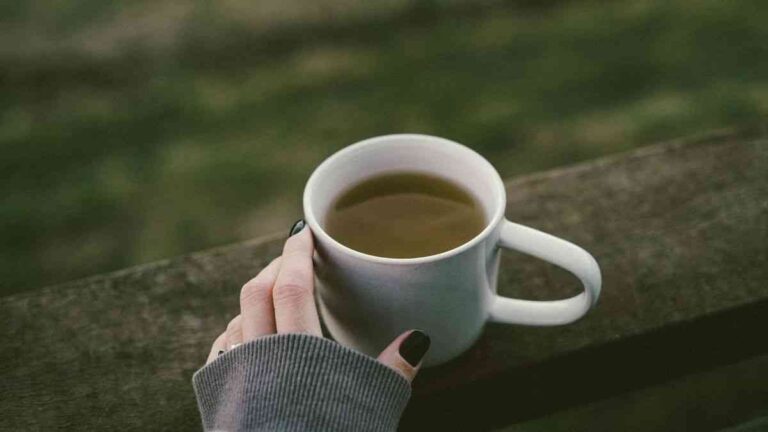 The influence of green tea on obesity: a white cup filled with green tea, held by a woman's hand. Photo: Valeriia Miller / Unsplash.