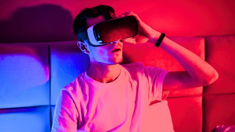 Are we living in a simulation: a man in VR goggles sits on a couch, red and blue lighting. Photo: Frimufilms / Freepik