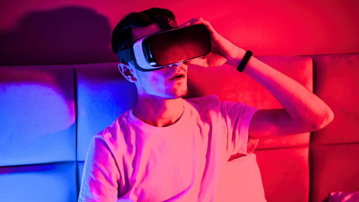 Are we living in a simulation: a man in VR goggles sits on a couch, red and blue lighting. Photo: Frimufilms / Freepik