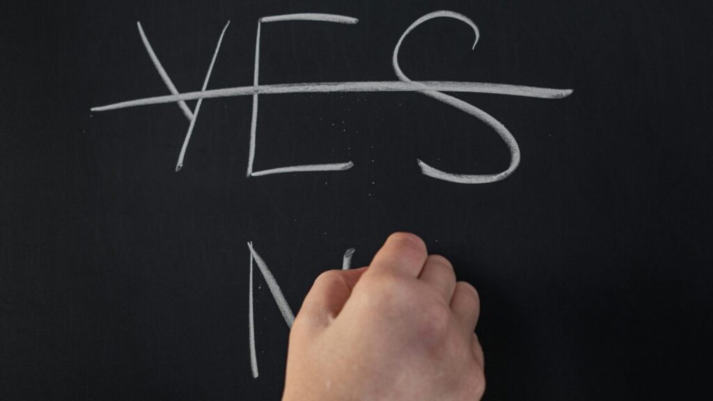 Crossed-out word YES and a hand writing NO, as a symbolic image of critical thinking.