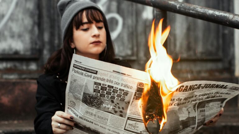 A young woman holding a burning newspaper.