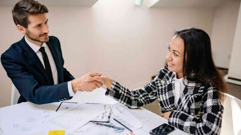 A man and a woman are sitting at a table and shaking hands.