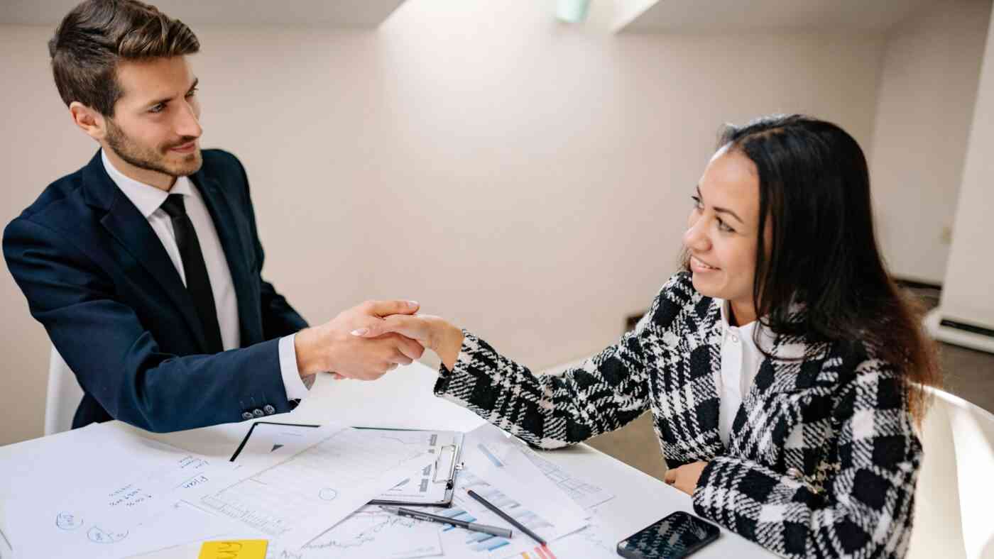 A man and a woman are sitting at a table and shaking hands.