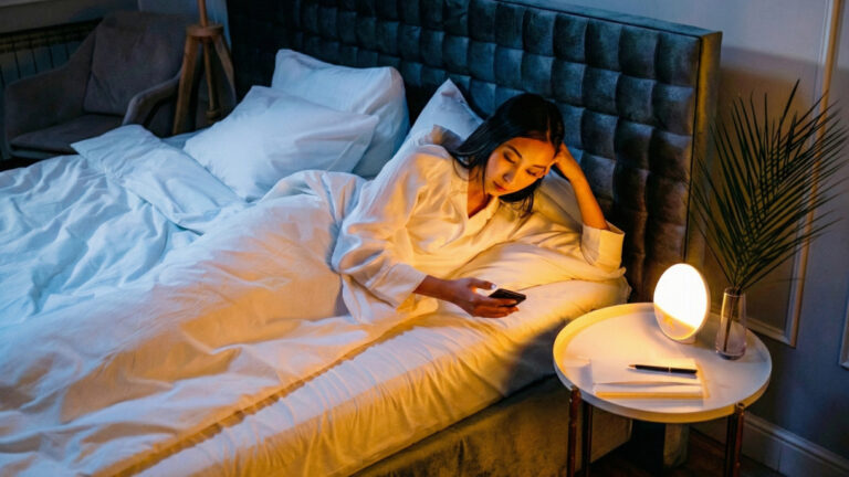 Woman lying in bed at night, staring at her phone screen, unable to sleep due to recurring negative thoughts in the brain.