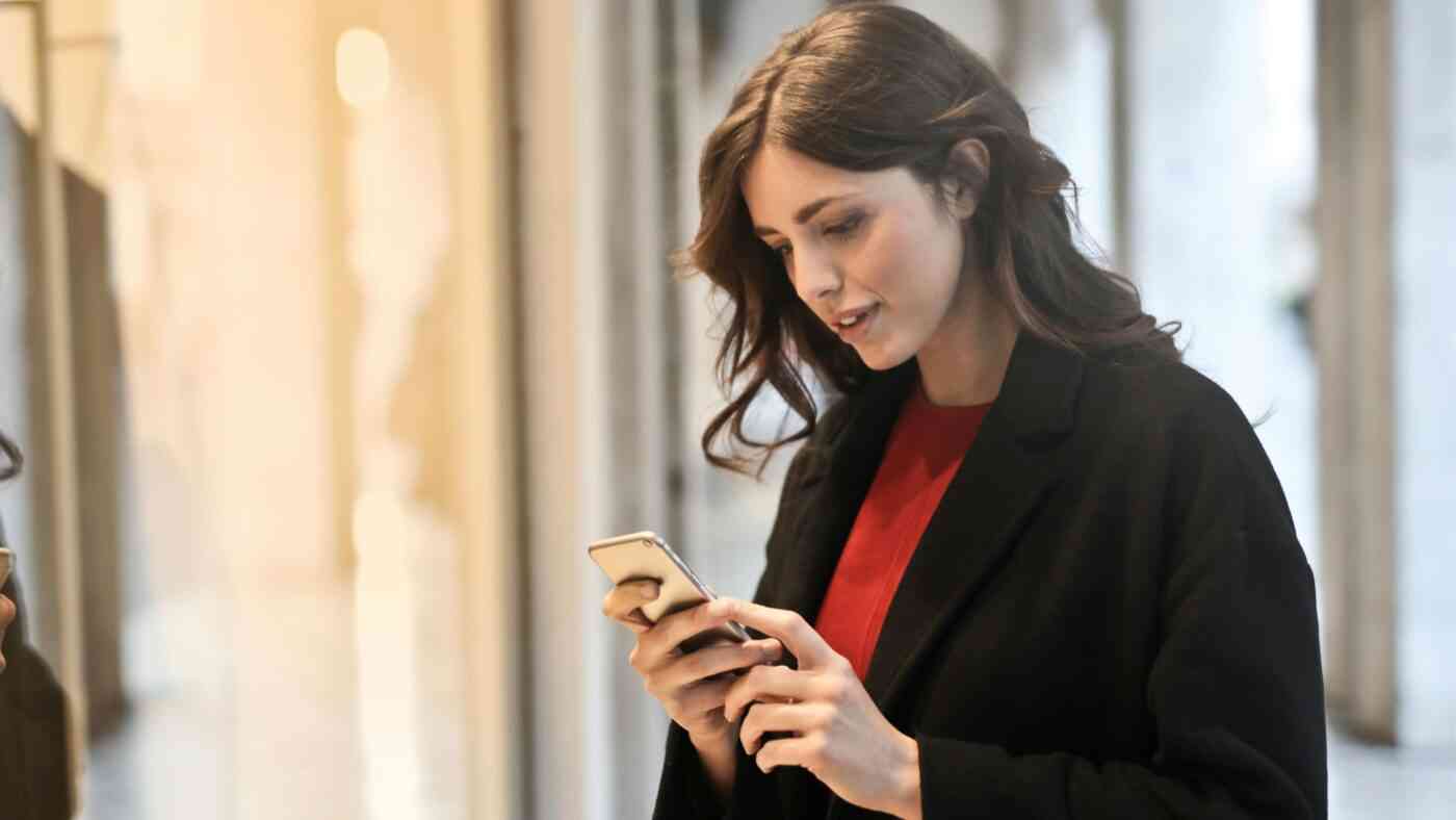 A woman in a black coat holding a cell phone, potentially interacting with AI chatbots while on the move.