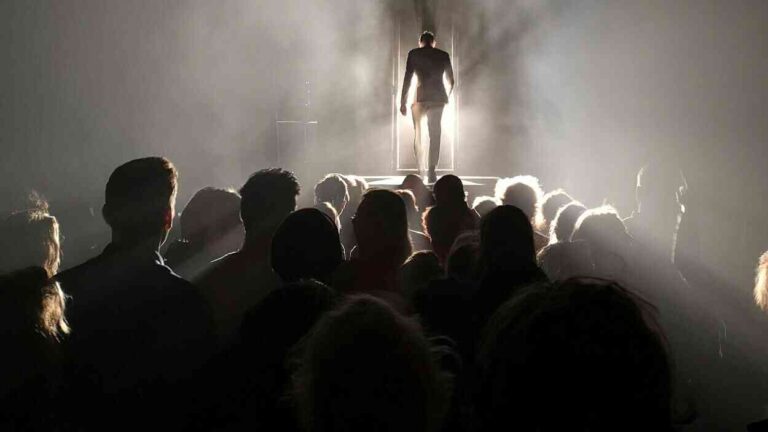 A figure standing in the light before a crowd symbolizes power built on fearmongering. This illustrates the techniques of manipulation and emotional influence that allow for the subjugation of a collective without the use of force.