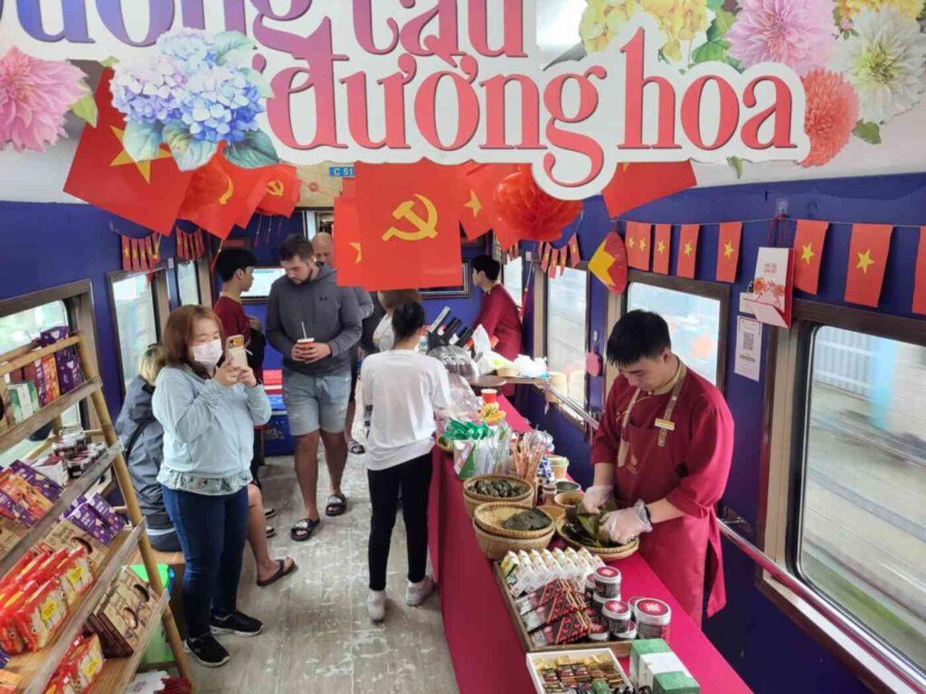 A vendor stall on a Vietnamese train decorated with red flags bearing the hammer and sickle — an everyday image of capitalism in Vietnam.