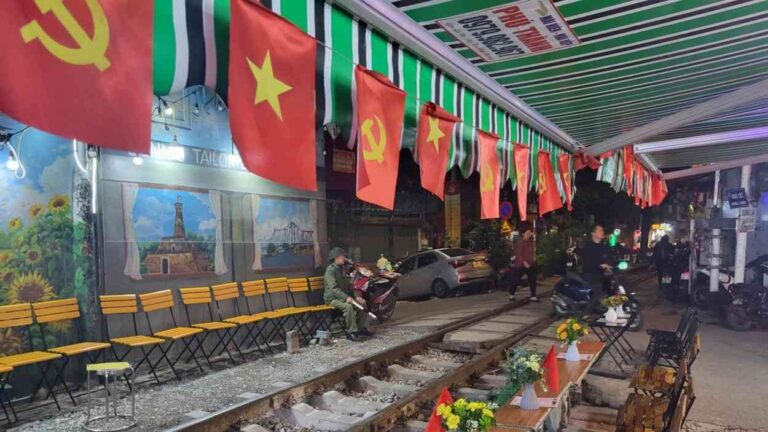A street in Hanoi with red flags bearing the hammer and sickle above railway tracks — a symbolic image of capitalism in Vietnam.