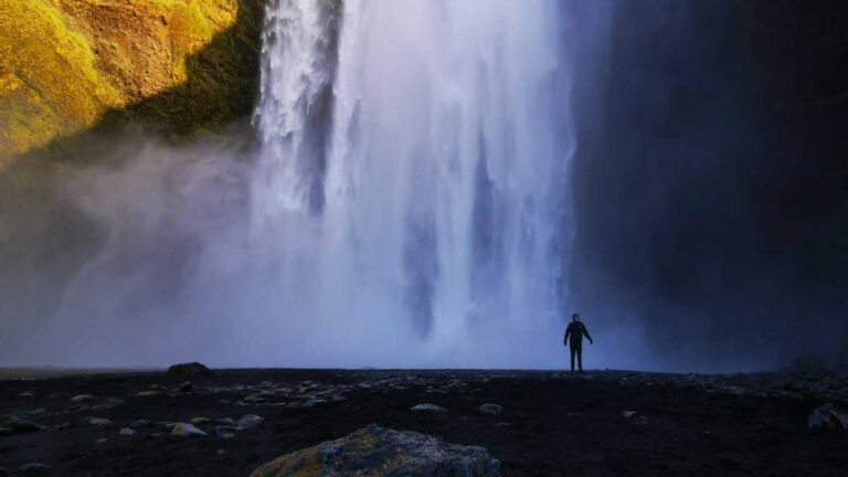 The world’s largest waterfall: a person stands alone at the base of a towering waterfall.