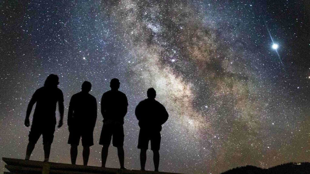 The structure of the world: four men standing on a hill, looking up at the starry sky — contemplating the ancient Greek arche.