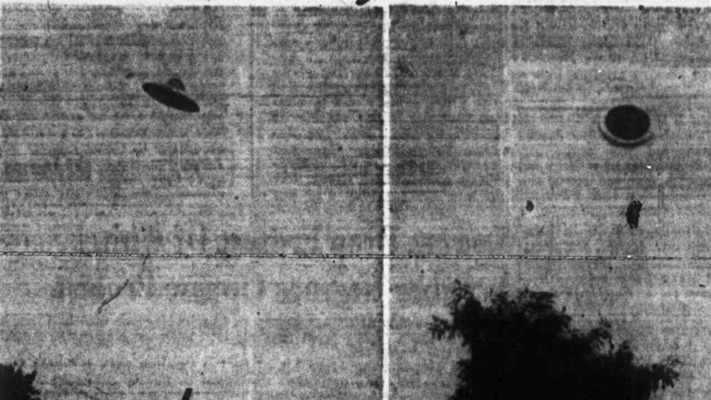 A blurry photo of two objects resembling unidentified flying objects seen over a landscape.