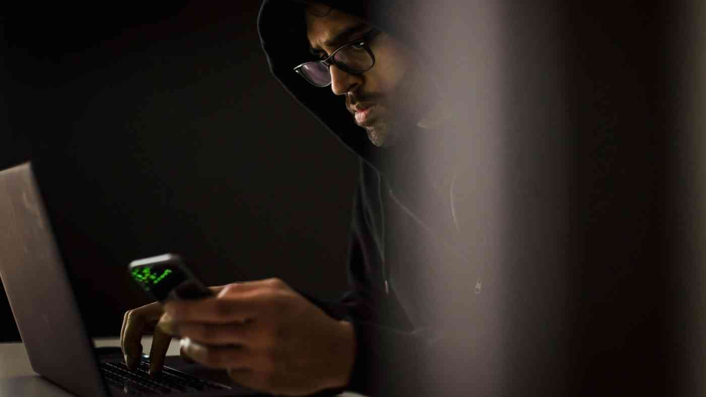 A hooded man sitting at a computer illustrates the relationship between the masculinity crisis and the manosphere online.