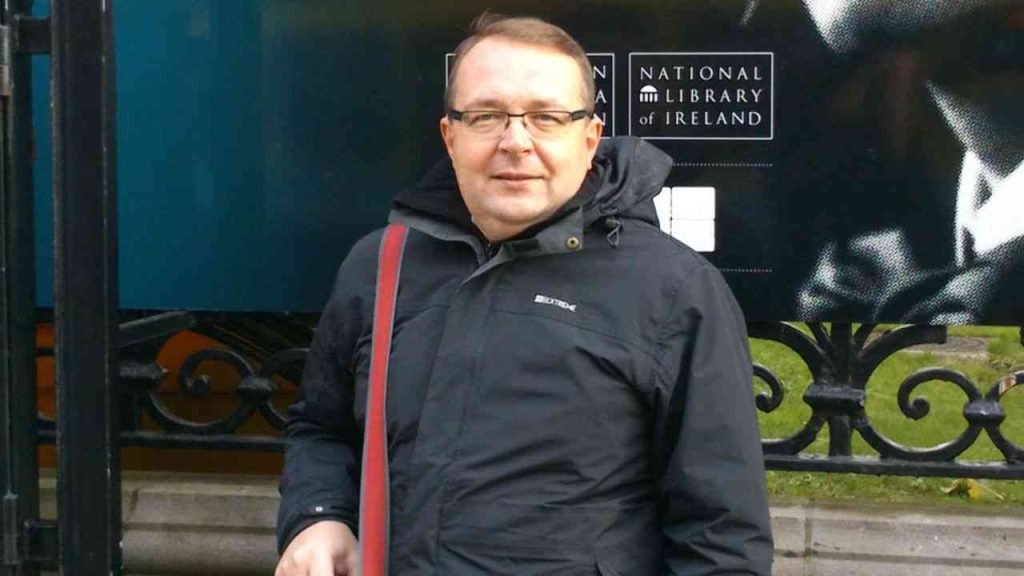 Piotr Gociek. The photo shows a man in a black jacket posing against a dark wall.
