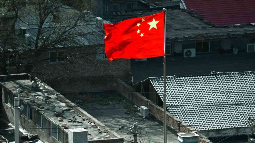 Close-up of the Chinese flag waving in the wind, with old grey buildings in the background. That is where a new Evil Empire is taking shape.