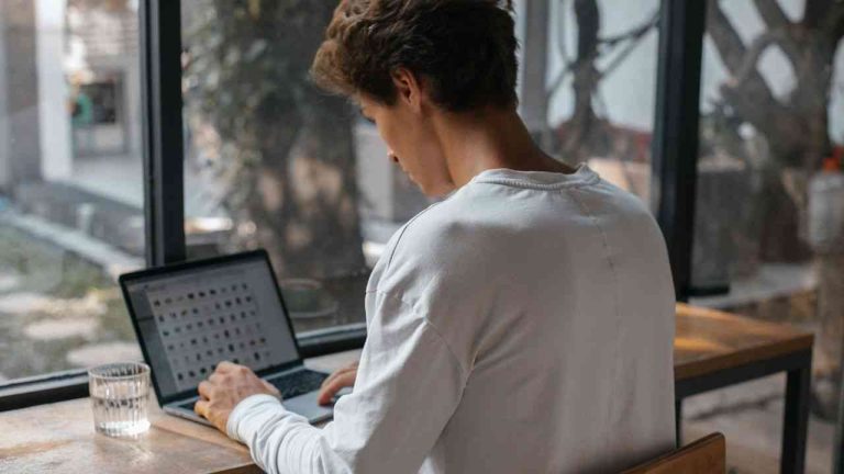 A young man in a white long-sleeve shirt sits at his computer, browsing images on a popular adult platform.