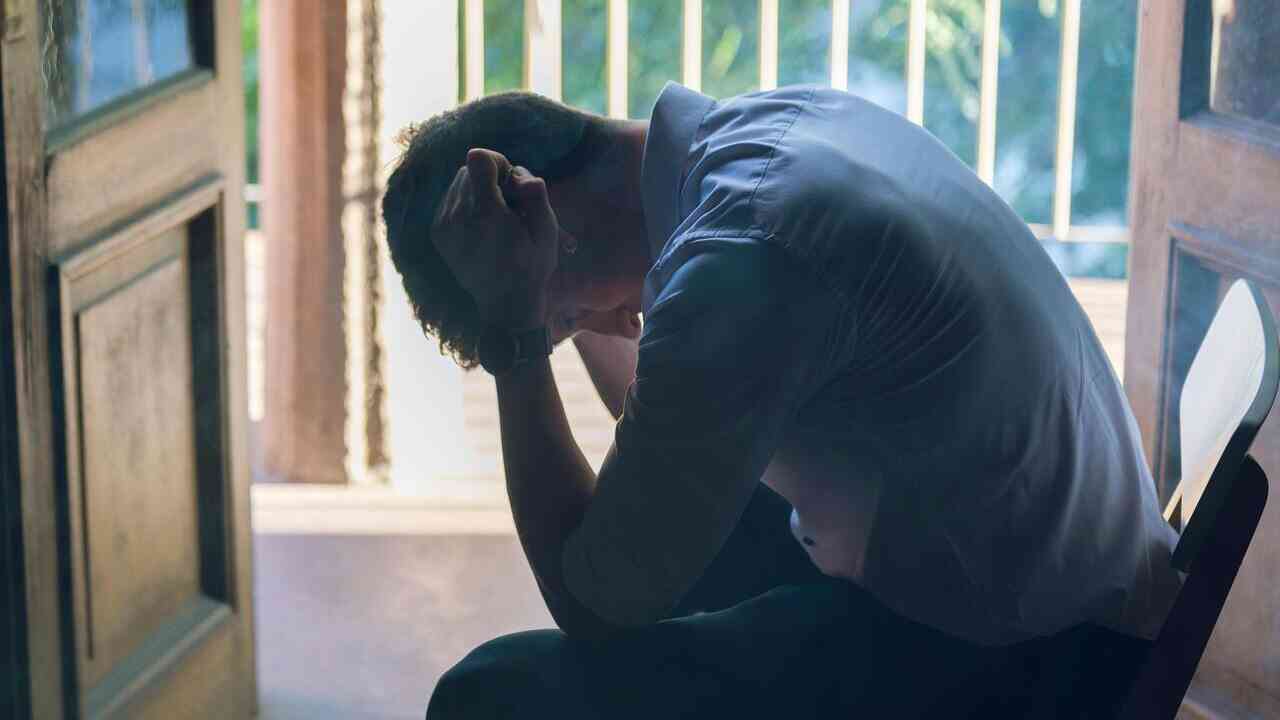 A man sits with his head bowed and his hand on his forehead, absorbed in pain and suffering—a reflection on why we feel pain and on the meaning of human suffering.