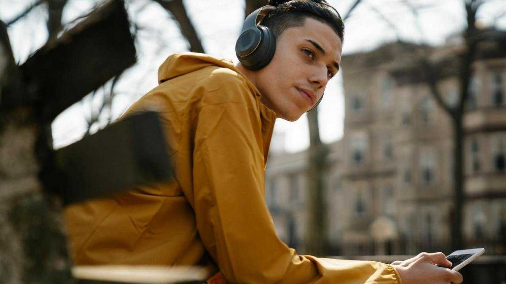 Audiobooks: a young man wearing headphones sits on a bench by the street