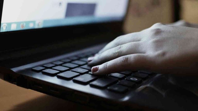 A close-up of an open laptop, with a woman’s hand on the keyboard, unaware of how fake news spreads.