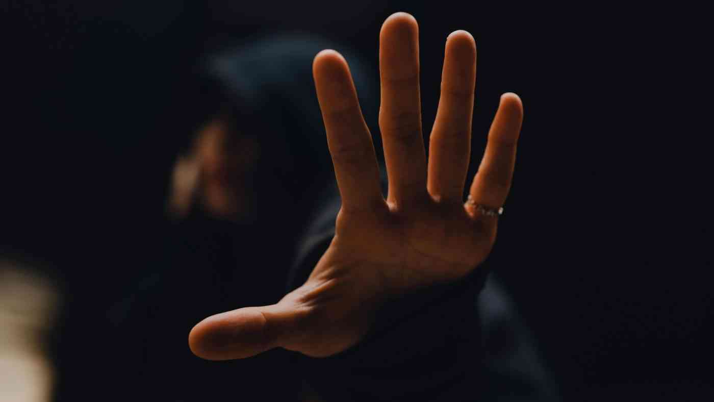 A man shielding his face with his hand, defending himself from an attack. The obligation to respect the limits of self-defense has been debated for years.