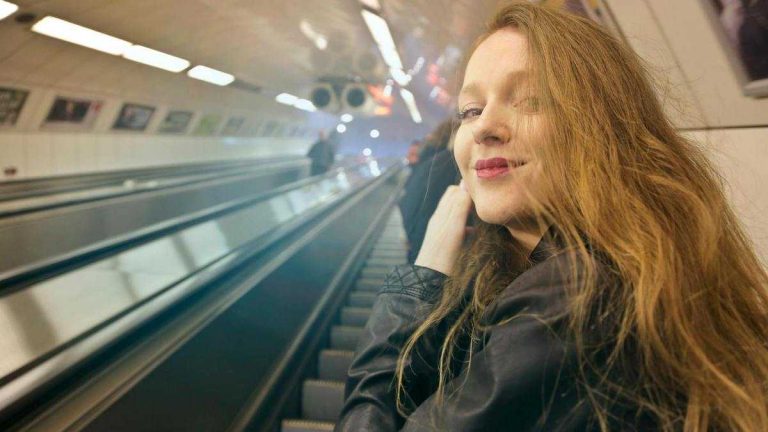 Stoic lifestyle: a smiling woman with long hair looks into the camera while standing on an escalator