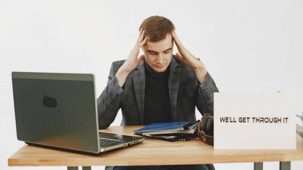 Stoic lifestyle: a man sits at a desk with a laptop and documents, holding his head in his hands