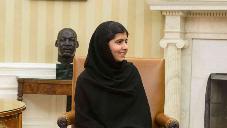The image shows a medium close-up of a woman in a black hijab, looking to the side as she speaks about what perseverance really means.