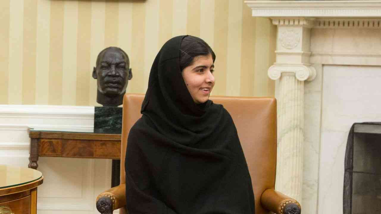 The image shows a medium close-up of a woman in a black hijab, looking to the side as she speaks about what perseverance really means.