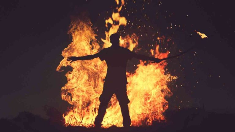 A man against a backdrop of fire, illustrating how the fight against evil can distort a noble cause.